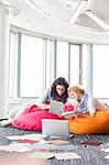 Businesswomen using tablet PC while relaxing on beanbag chairs at creative office
