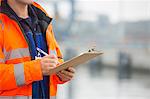 Midsection of mid adult man writing on clipboard in shipping yard