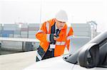 Middle-aged man talking on walkie-talkie while using laptop in shipping yard