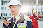 Male worker using walkie-talkie with colleague in background at shipping yard