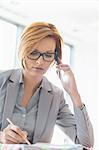 Young businesswoman on call while writing at desk in office