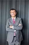 Portrait of smiling mature businessman standing arms crossed against wall