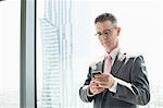 Mature businessman using cell phone by window