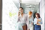 Young businesswoman on call with colleagues in background at office corridor