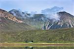 Small white solitary crofters cottage nestling below mountain range reflected in waters of the loch, Isle of Skye, Inner Hebrides, Highlands and Islands, Scotland, United Kingdom, Europe