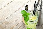 Fresh mojito cocktail and bar utensils on wooden table with copy space