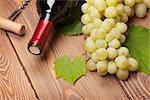 Red wine bottle and bunch of white grapes on wooden table background