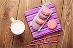 Colorful macaron cookies and cup of milk on wooden table background