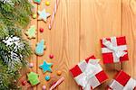 Christmas wooden background with snow fir tree, gingerbread cookies and gift boxes. View from above with copy space