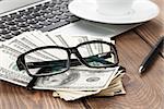 Office table with pc, coffee cup and glasses over money cash closeup