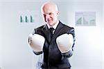 smiling self confident businessman challenging the observer with a pair of boxing gloves