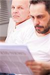 serious man with a friend reading newspaper in a living room