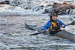 senior male paddling sea kayak through river rapids