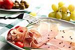 Delicious prosciutto plate with olives, tomatos, grapes and a fork.