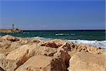 Rock sea wall with small lighthouse on the Mediterranean Sea in Herzliya Israel near Jaffa and Tel Aviv with view of the beach.