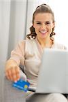 Portrait of happy young housewife with laptop holding credit card