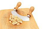 Macadamia nuts with a rocking knife on a wooden chopping board, isolated on a white background