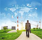 Businessman walks on road. Rear view. Industrial zone, grass field and sky with virtual elements. Business concept