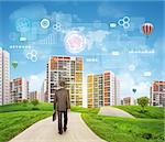 Businessman walks on road. Rear view. Buildings, grass field and sky with virtual elements. Business concept