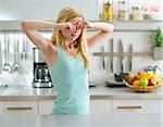 Young woman standing in in kitchen and rubbing eyes after sleep