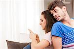 young woman on a sofa in her living room using her mobile phone ignoring his boyfriend