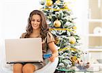 Happy young woman with credit card using laptop near christmas tree