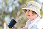 Woman in hat  sitting  in nature and holding a  cup of coffee