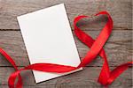 Valentines day heart shaped red ribbon and blank greeting card over wooden table background