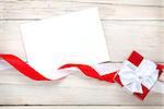 Greeting card and gift box with ribbon over white wooden table background