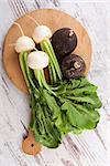 White and spanish radish on round wooden cutting board on white wooden textured background, top view. Culinary healthy vegetable eating.