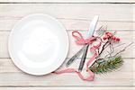 Empty plate, silverware and christmas decor. View from above over white wooden table background