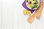 Fresh healthy salad and kitchen utensils over white wooden table. View from above with copy space