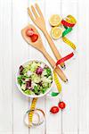 Fresh healthy salad, utensils and tape measure over white wooden table. View from above