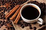 roasted coffee with cup of black coffee and cinnamon sticks closeup