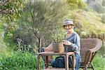 Woman sitting on wecker bench in nature and having a pot with plant