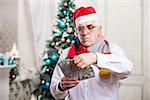 Senior man in Santa's hat holding money over Christmas background