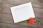 Blank photo frame and orange gerbera on wooden table background