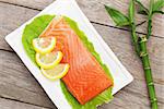 Fresh salmon fish with lemon and salad leaves on wooden table