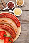 Various grilled sausages with condiments and tomatoes on cutting board