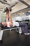Fit man lifting dumbbell lying on the bench at the gym