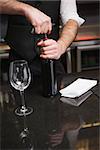 Handsome waiter opening a bottle of red wine in a bar