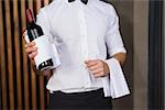 Handsome waiter holding a bottle of red wine and a towel in a bar