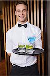 Cheerful young waiter holding tray with cocktails in a bar