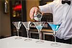 Bartender pouring blue alcohol into cocktail glass in a bar