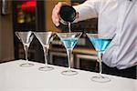 Bartender pouring cocktail into glasses in a bar