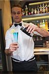 Handsome bartender serving blue cocktail in a bar