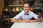 Smiling bartender having glass of red wine in a bar