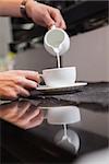 Barista pouring milk into cup of coffee in a cafe