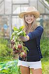 Happy blonde showing home grown vegetables at home in the garden