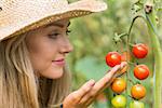 Pretty blonde looking at tomato plant at home in the garden